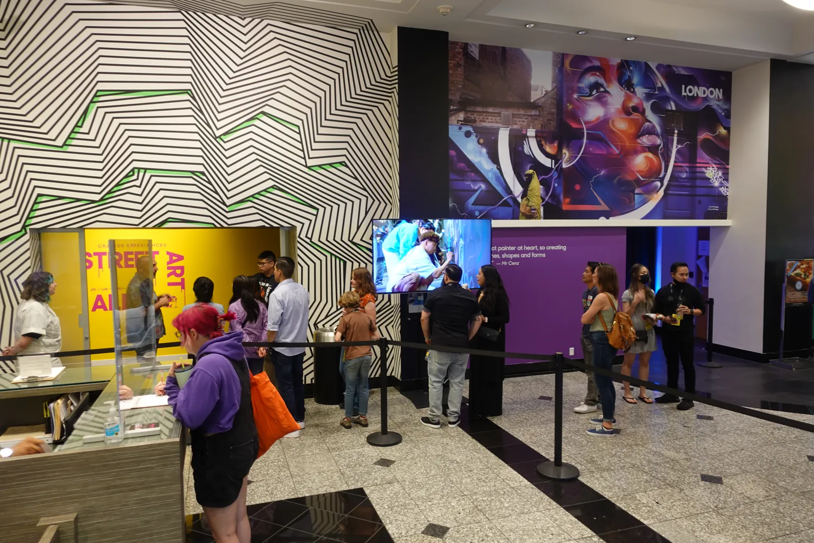 Guests lining up at a lobby ticket counter beside black and white striped walls