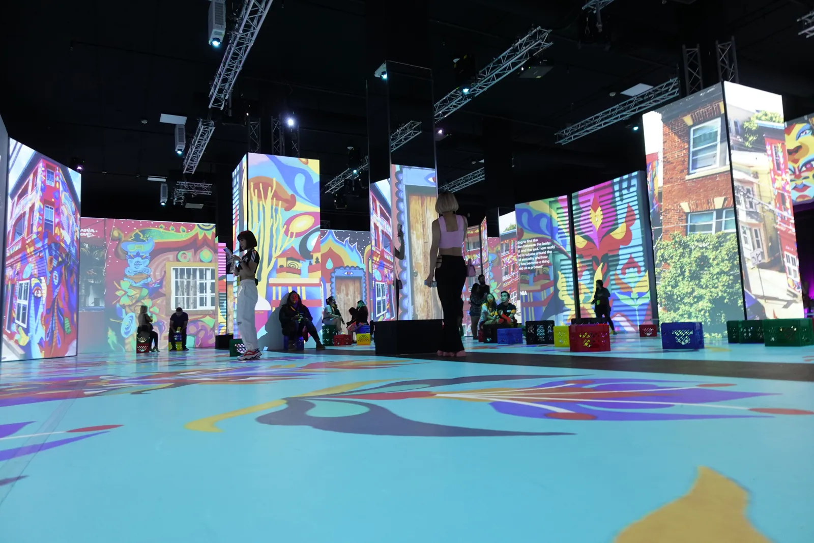 Guests sitting on milk crates among colorful projected panels and a blue floor