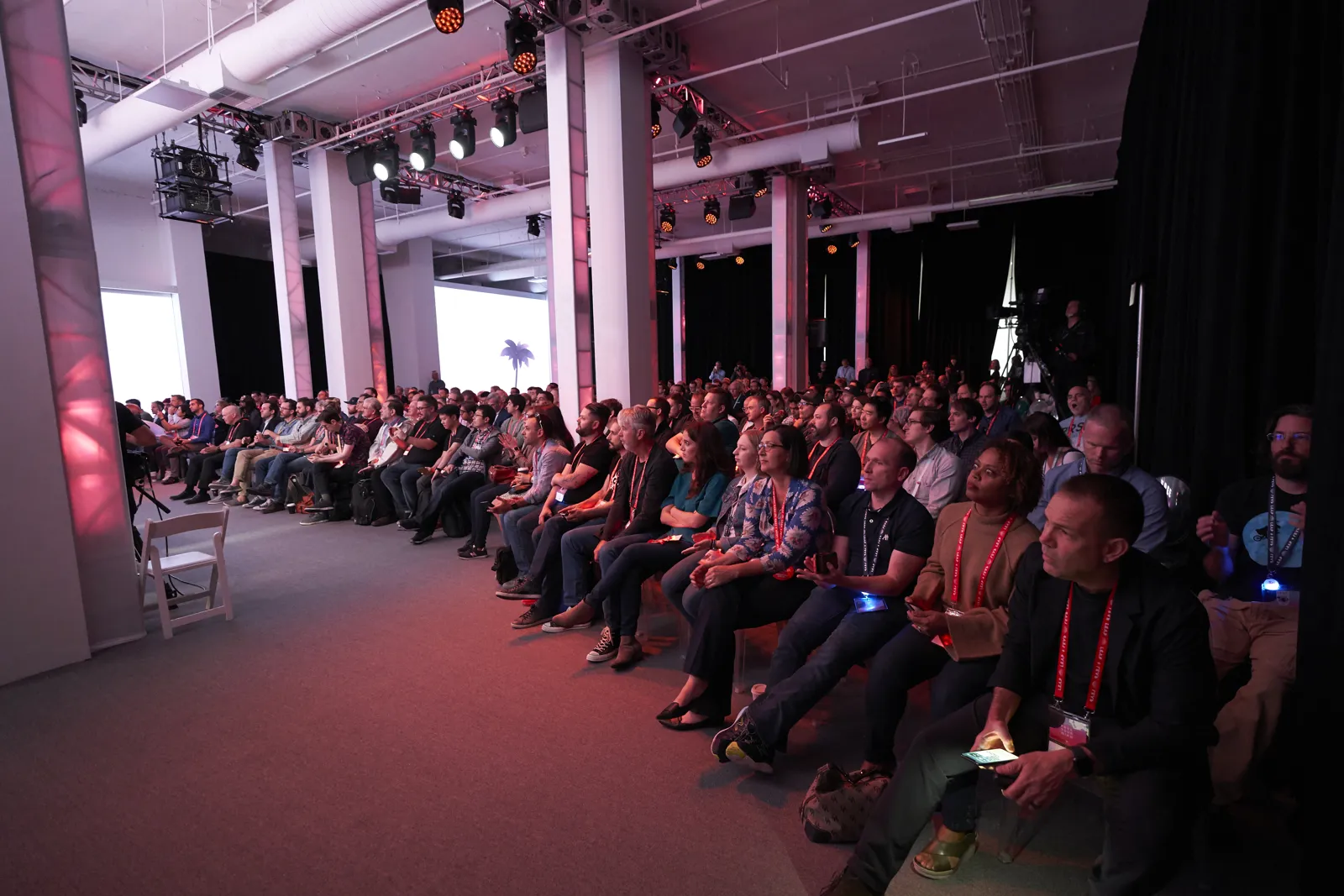Seated audience watching a presentation in a dark event hall with overhead truss lighting