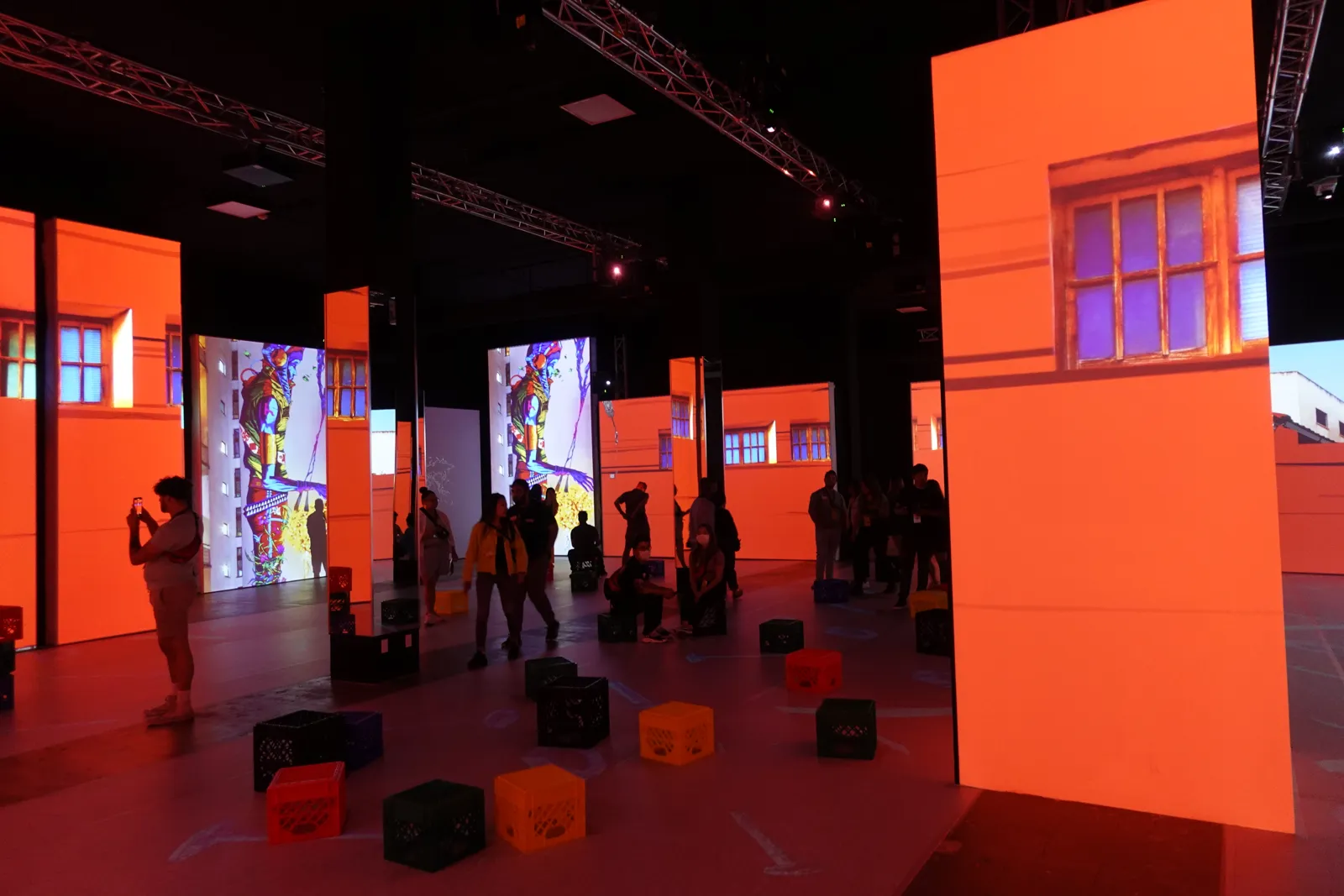 Dark hall lit orange by projections, with crate seats and visitors standing around