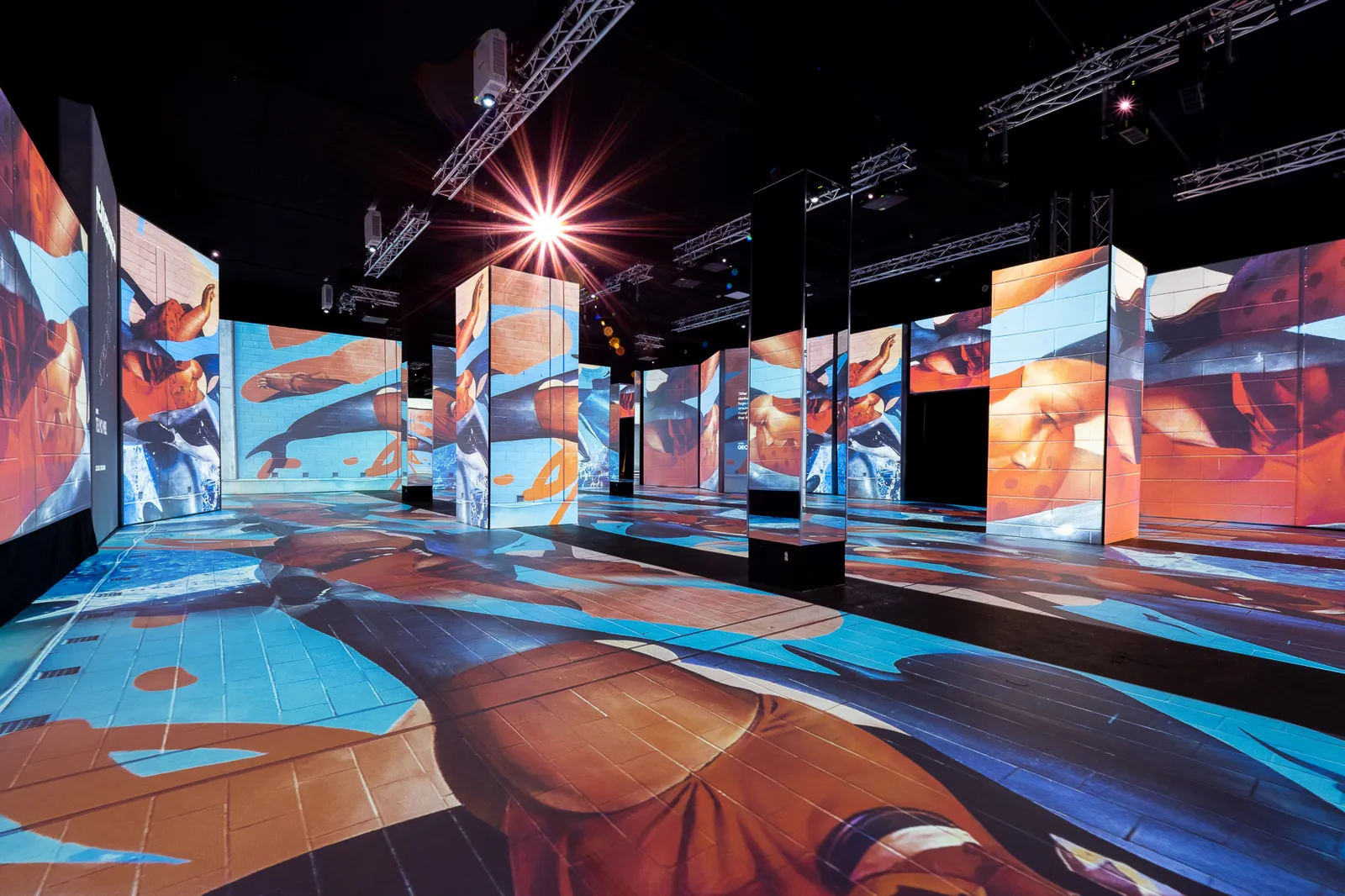 Projected mural artwork across tall panels and the floor of a dark exhibit hall