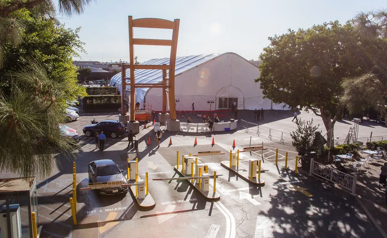Giant wooden chair sculpture beside a parking entrance and a large white tent