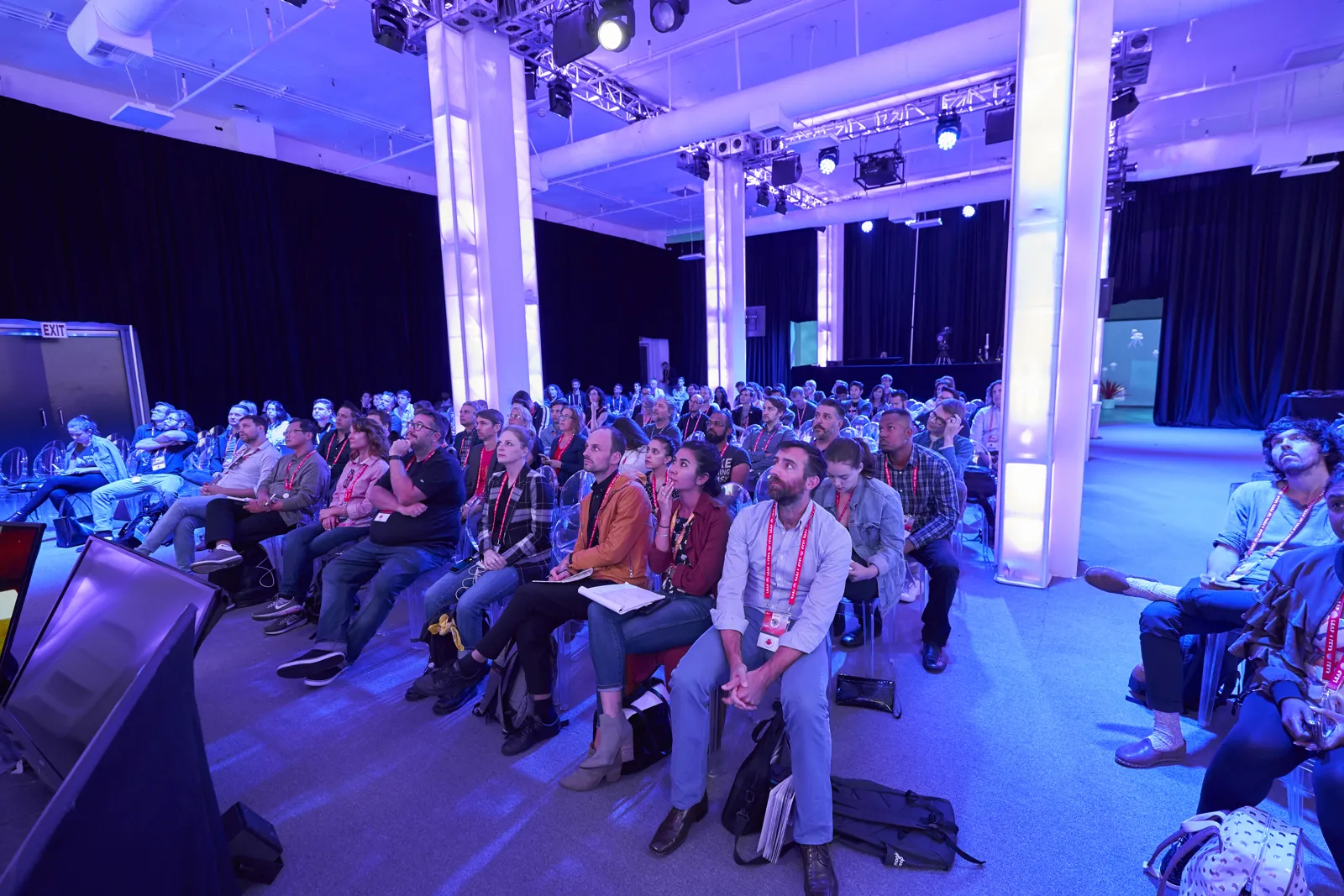Conference audience seated in rows under blue light in a large columned hall