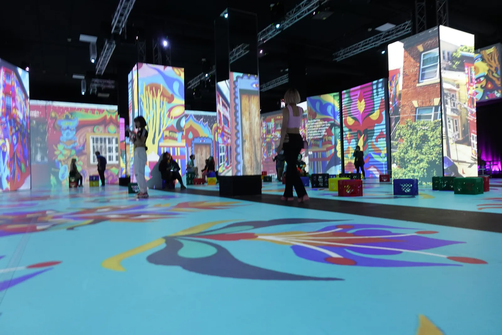 A teal floral floor projection and bright street art panels fill an exhibition hall