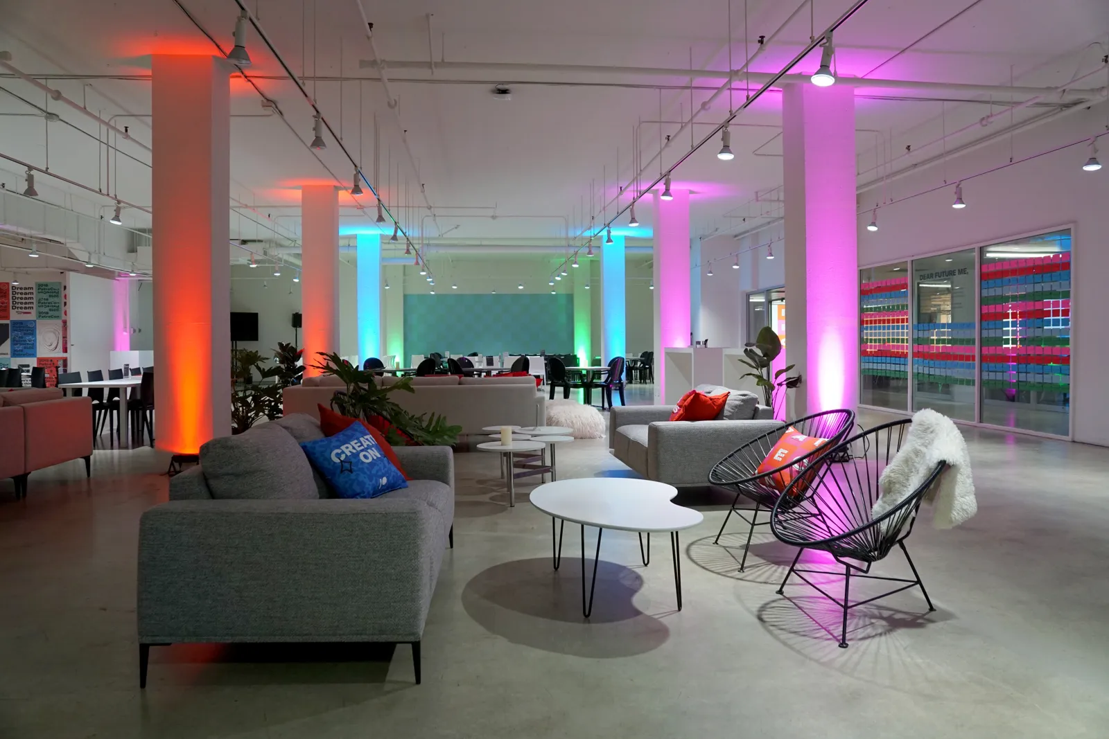 Lounge with grey sofas and rope chairs beside pillars lit pink and teal