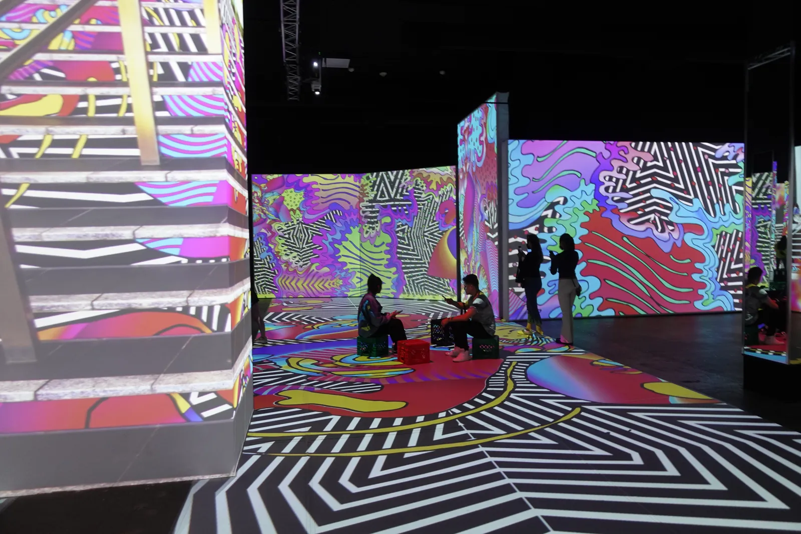 Guests seated on crates surrounded by bright swirling projected patterns