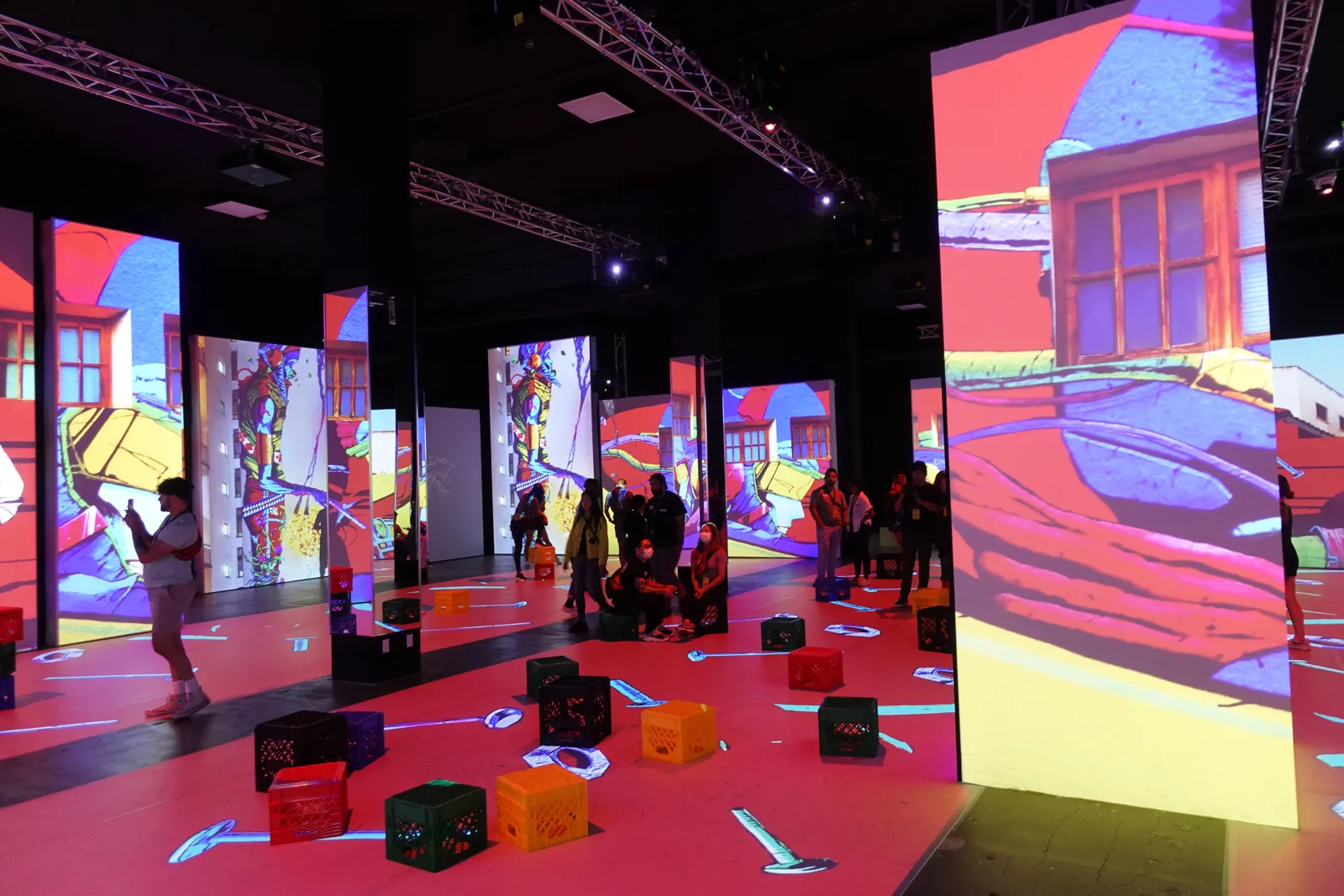 Colored milk crate seats on a red projected floor beside a giant house facade image