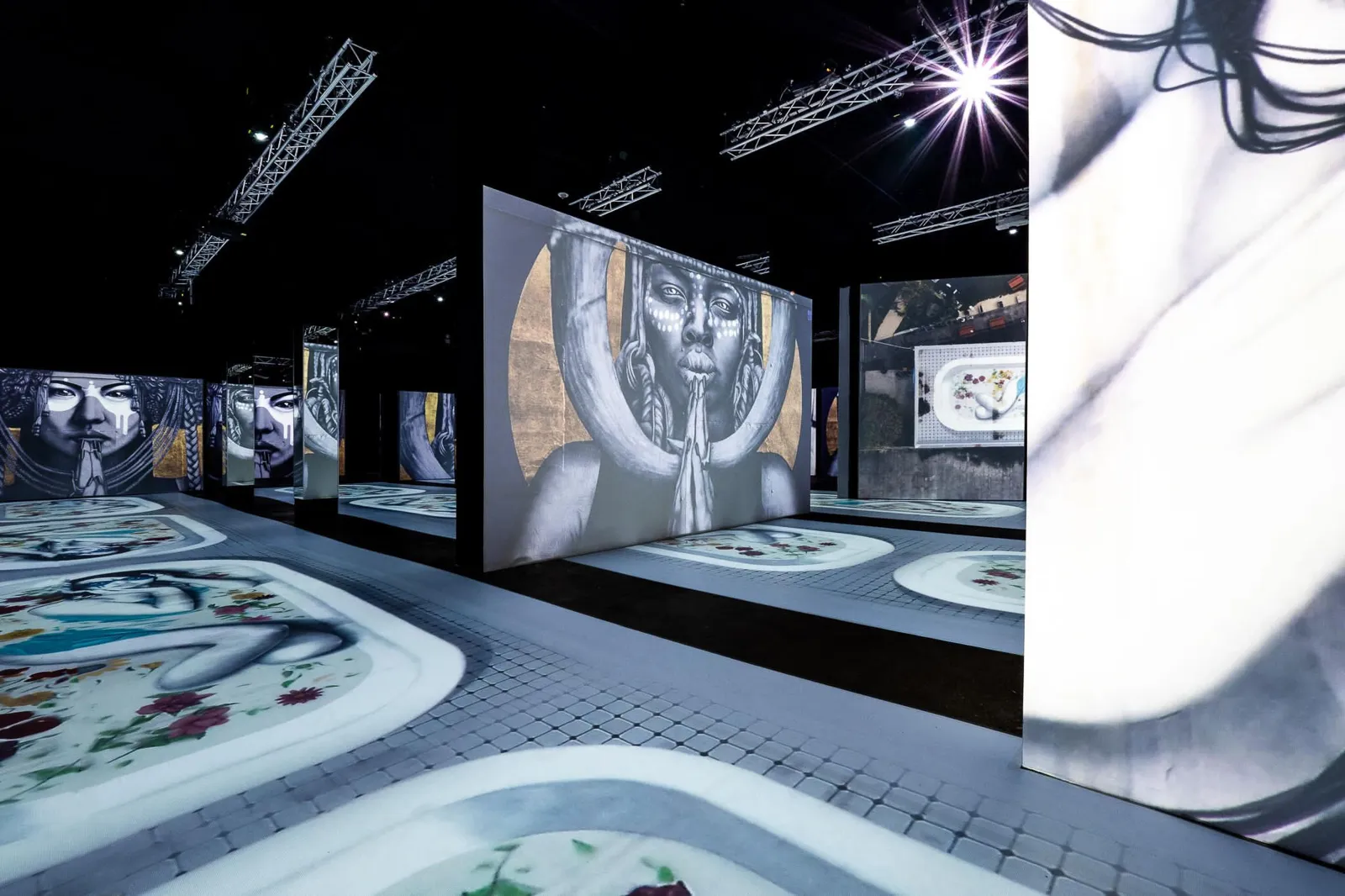 Dark exhibition hall with black and white artwork projected on freestanding walls and floor