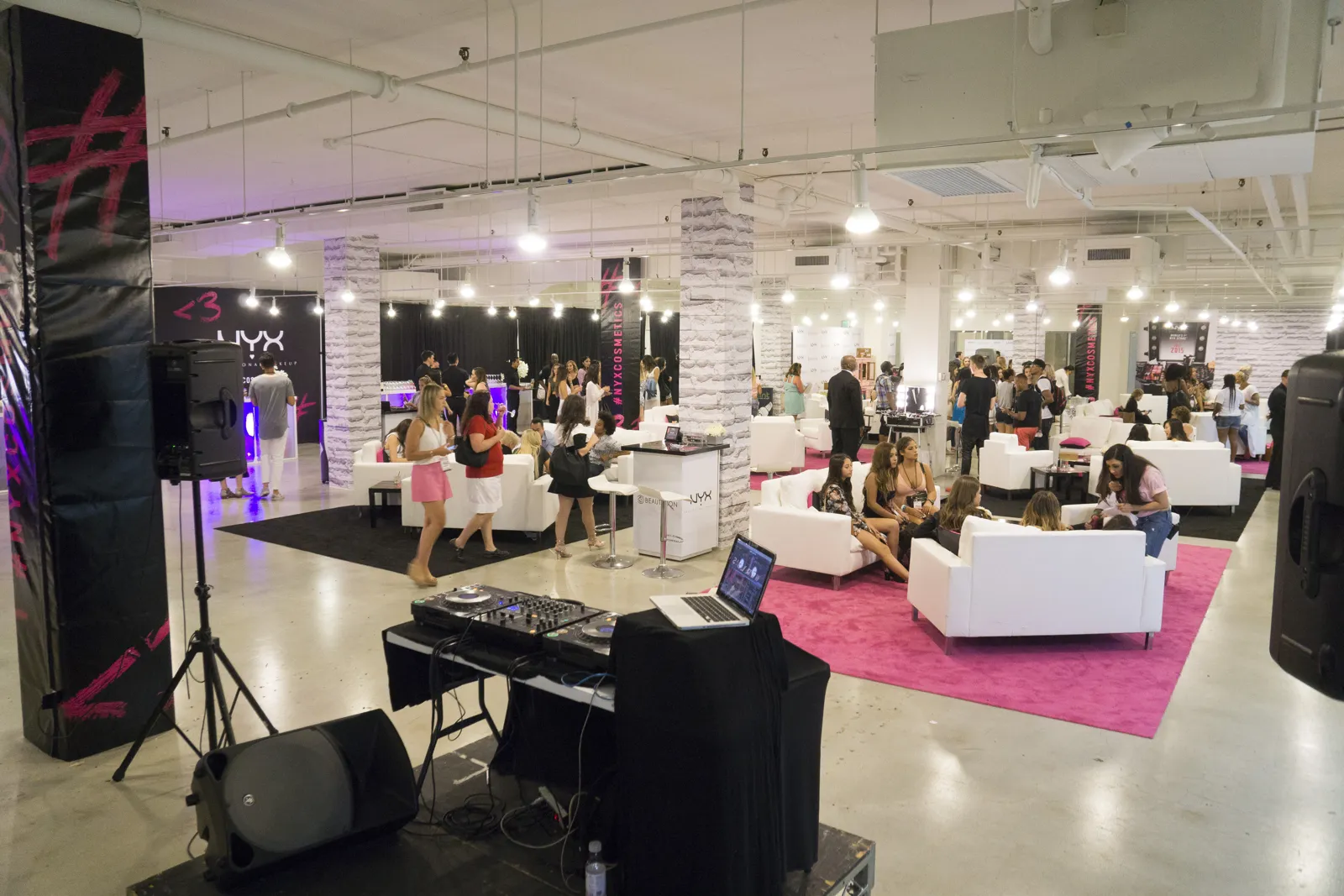 Bright hall with white sofas, a pink rug and a DJ setup as guests mingle