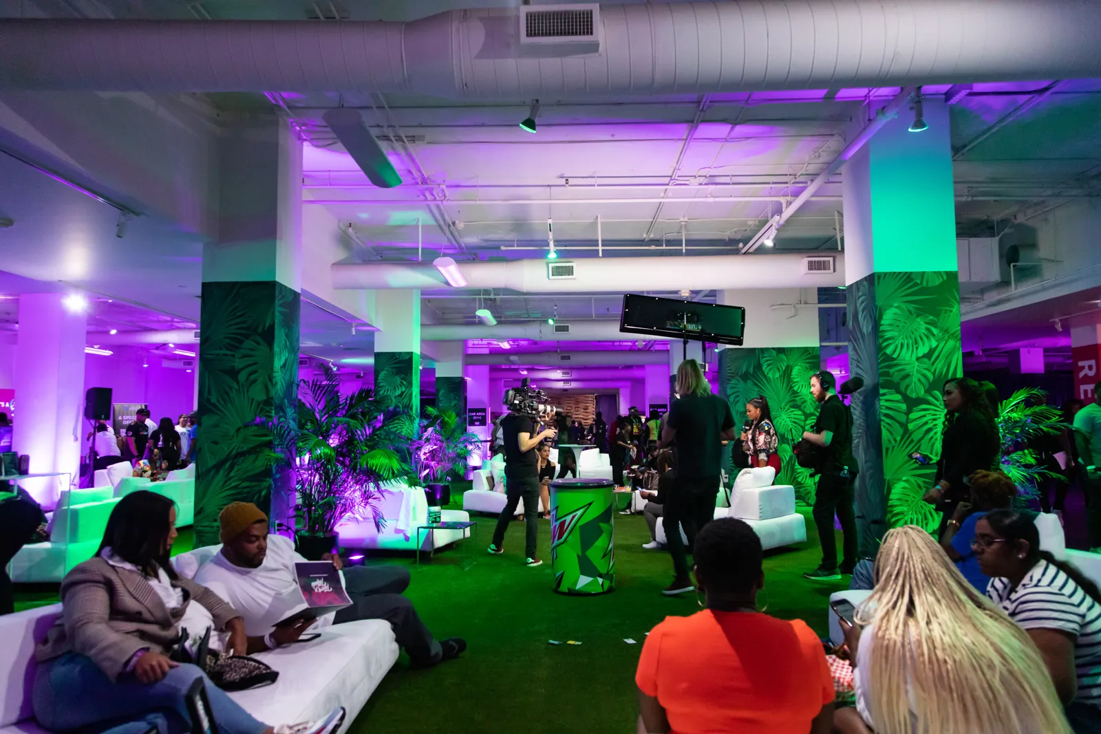 Guests relaxing in a lounge with green turf, tropical plants, white sofas and purple lighting
