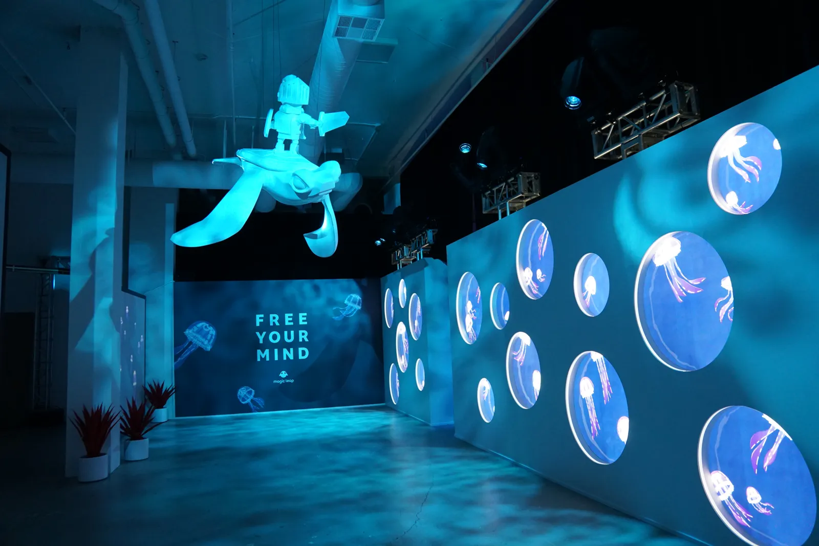 Teal lit activation with a suspended turtle sculpture and round jellyfish screens