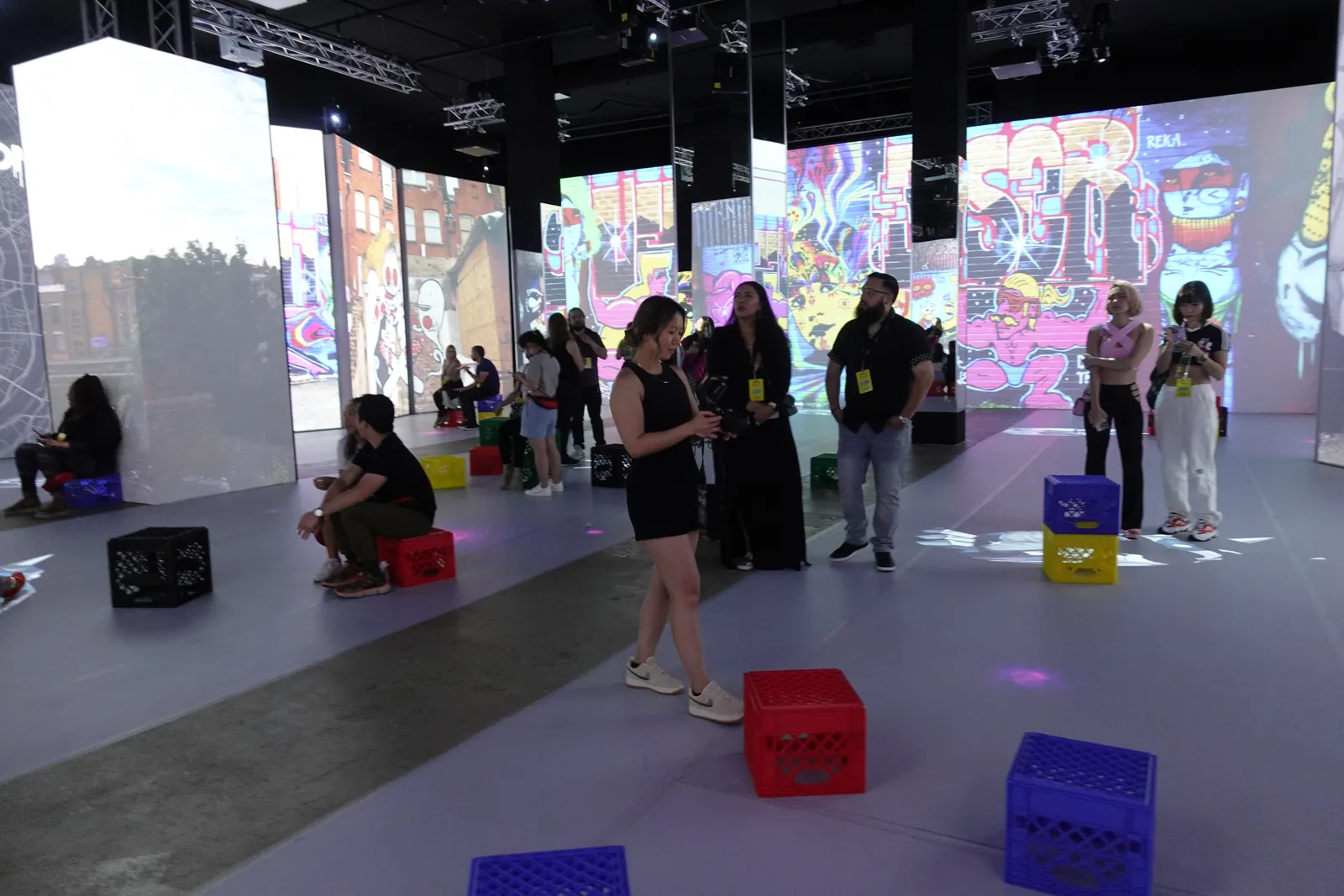 Guests mingle and sit on crates among projected art walls on a lavender floor