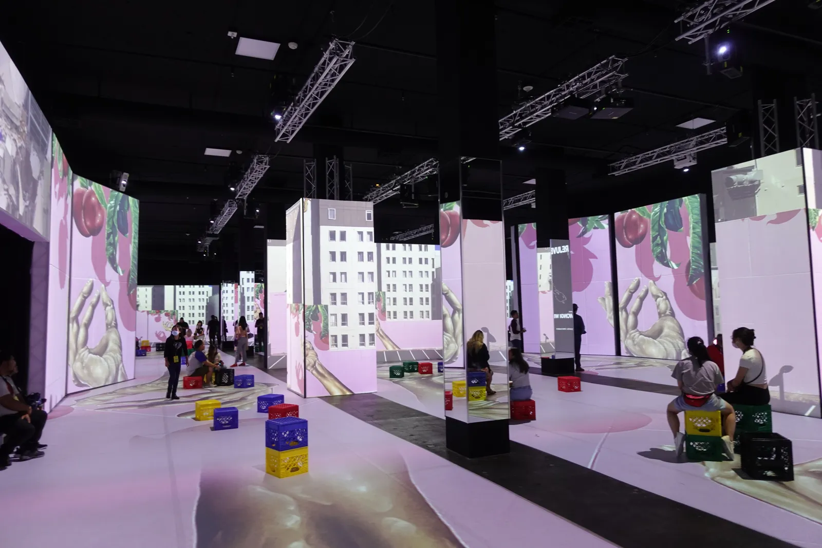 Bright projection hall with colorful crate seats and visitors resting between panels