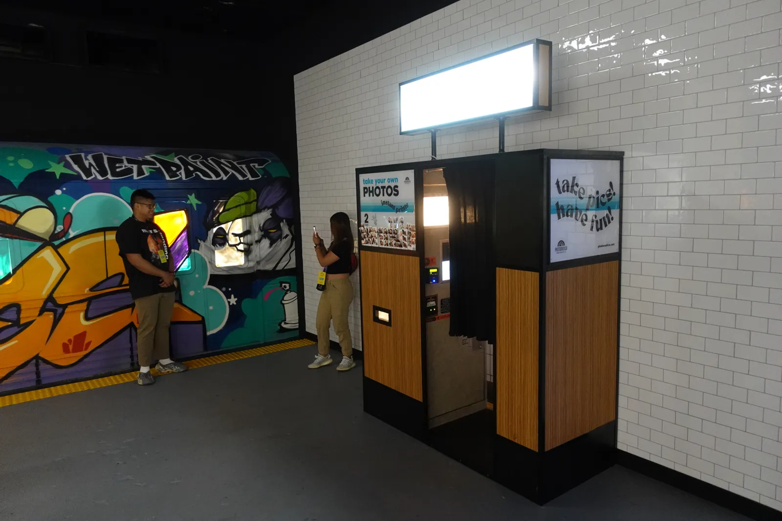 Vintage photo booth beside a white tiled wall and a graffiti subway car