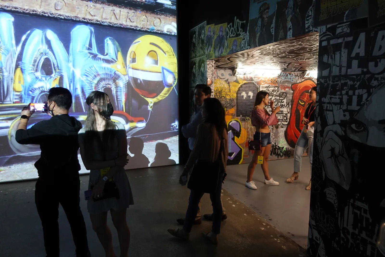 Guests photographing a large projected graffiti wall in a dim gallery