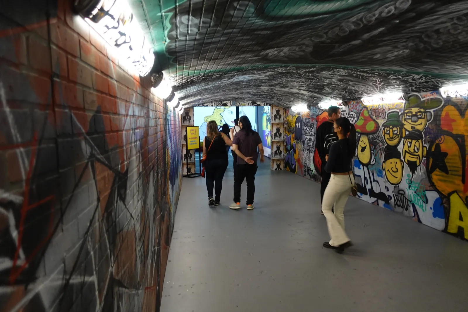 Guests walking through a narrow tunnel covered in graffiti murals