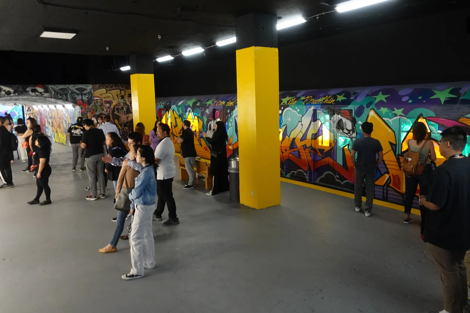 Guests walking through a hall lined with a long graffiti mural and yellow columns