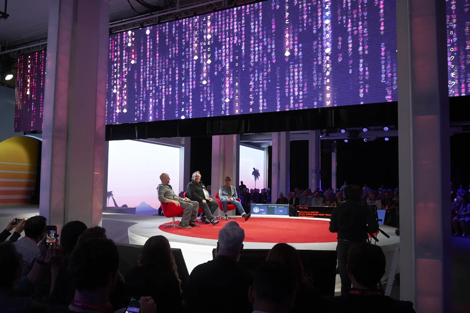 Audience watching a panel on a round red stage under a purple LED wall