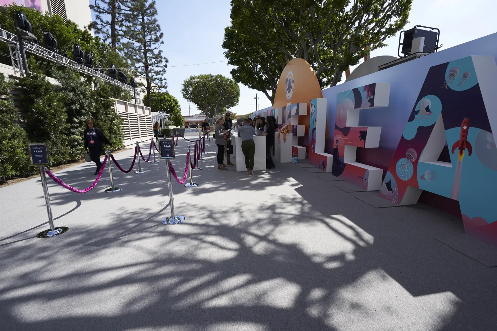 Outdoor entrance with giant letter sculptures, velvet ropes and stanchions in sunlight