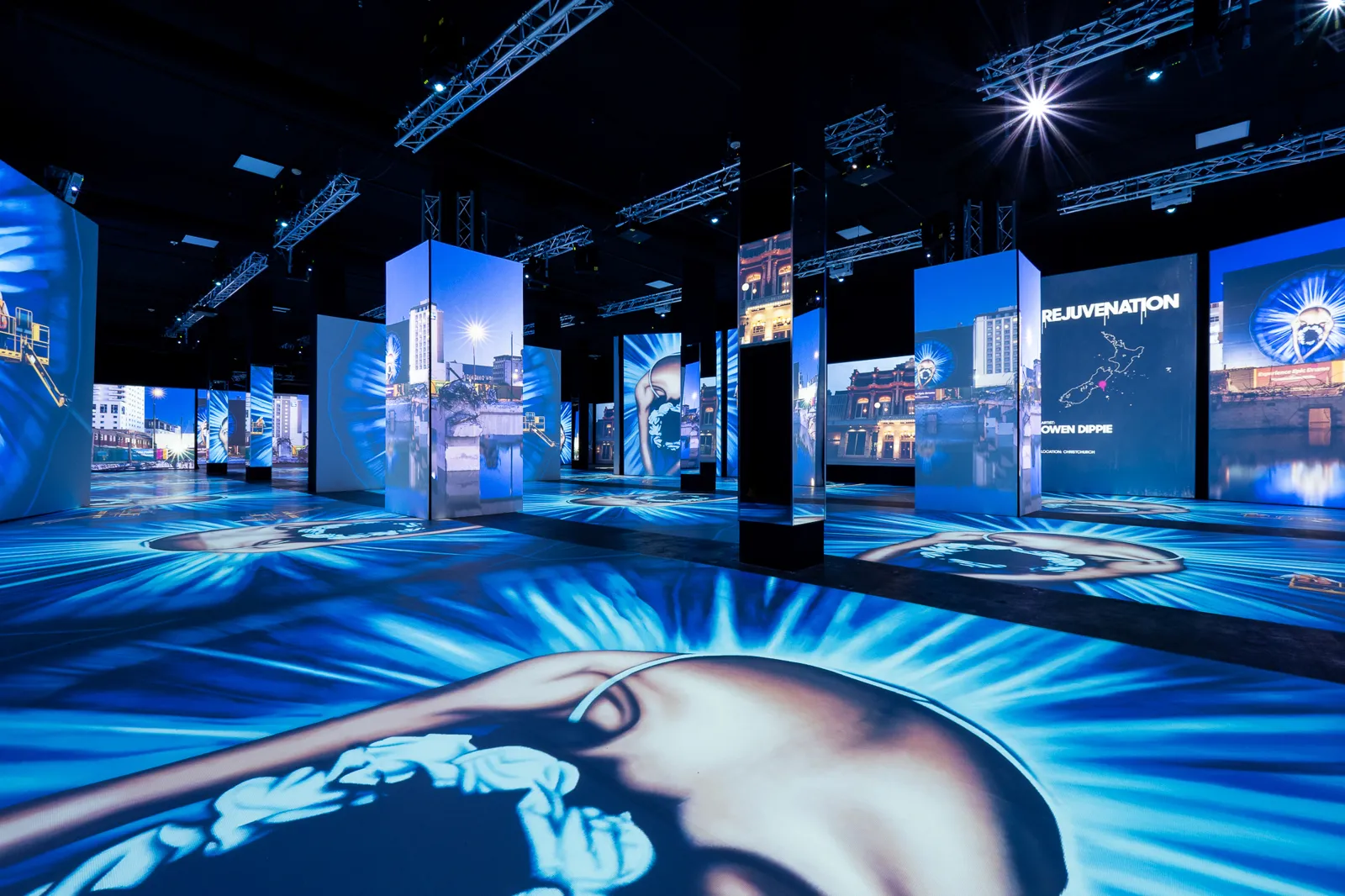 Blue toned projections of a giant face and city scenes in an empty hall