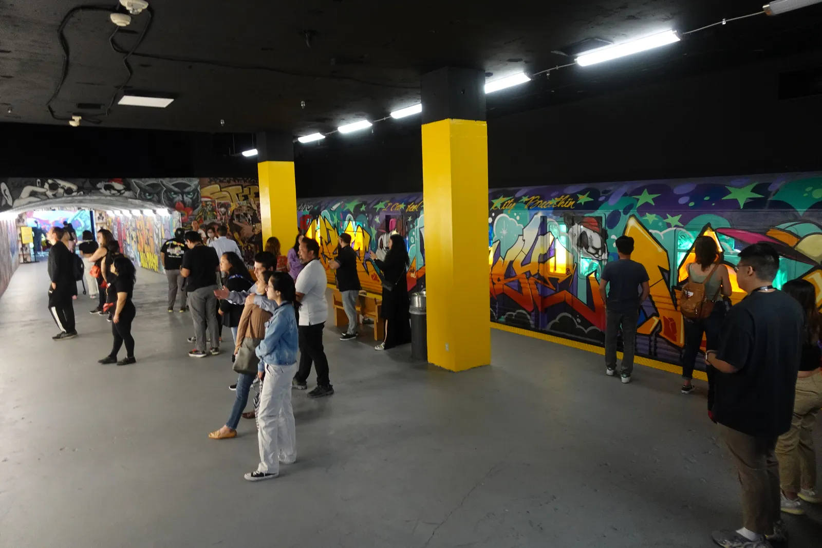 Visitors looking at graffiti murals along a wall with bright yellow pillars