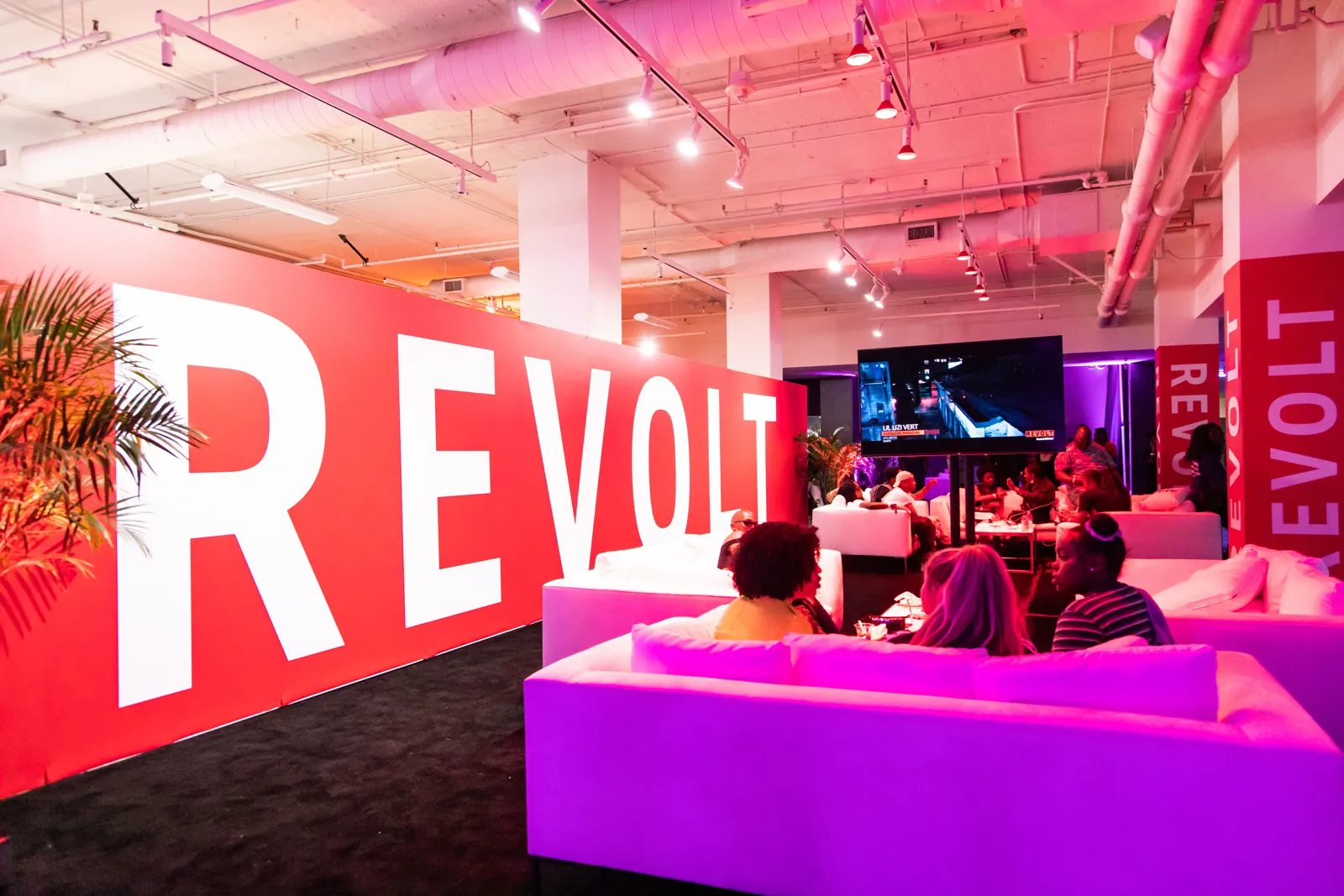 Pink-lit lounge with white sofas, guests and a large red wall graphic