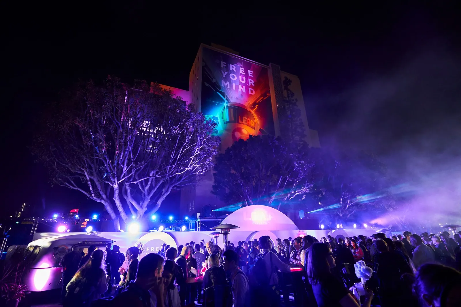 A crowd under lasers and a lit tree at a night event